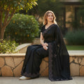 Woman wearing a ManasLifestyle.in black saree with delicate embroidery, sitting outdoors in a garden setting.